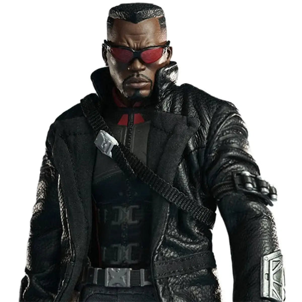 A black leather jacket with a high collar, worn by a man wearing red-tinted sunglasses and a black tactical vest. The jacket features silver metallic accents on the chest strap, belt, and sleeve.