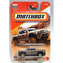 Matchbox 2024 Toyota Tacoma die-cast toy truck in its original blister card packaging, featuring a gray toy truck and a printed illustration of a tan truck on a desert background.