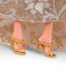 Close-up of doll feet wearing gold high-heeled shoes with a patterned dress.