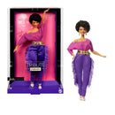 Barbie doll in a purple outfit with fringe and gold belt, next to its packaging.