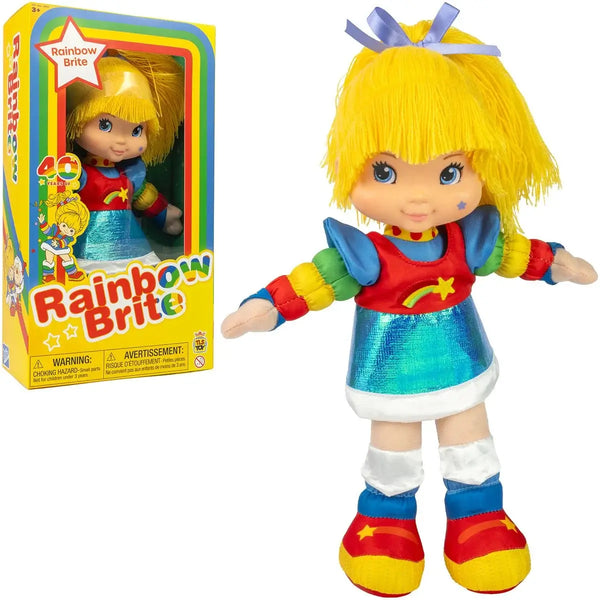 Rainbow Brite plush doll shown standing next to its retail box on a plain white background. The doll has bright yellow hair with a blue bow, a red and blue outfit with rainbow-colored arm bands, white socks, and red and yellow shoes.