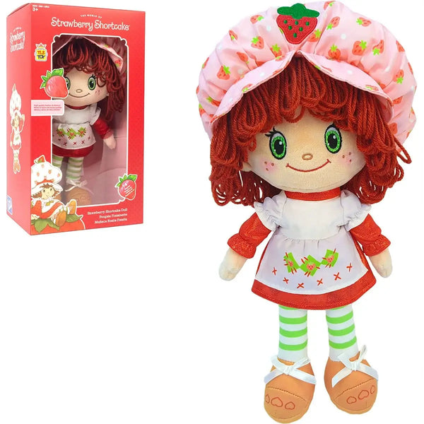 Strawberry Shortcake plush doll shown next to its red retail box on a white background. The doll has red curly hair, a pink strawberry-patterned bonnet, a white dress with red trim and green leaf embroidery, green-and-white striped tights, and tan shoes.