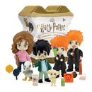 A set of Harry Potter character figurines and accessories displayed in front of their collectible capsule packaging. The figures include characters in black robes, a figure in a pink top, a figure in a green jacket, and a small white creature, along with themed accessories like a cauldron, wand, and potion bottles.
