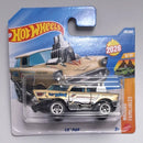 A Hot Wheels die-cast toy car in its original blister card packaging, featuring the 'Lil' Mad' vehicle. The toy car is tan and black with 'Lil' Mad' written on the side, set against a blue and orange card backing.