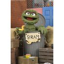 A collectible figurine of Oscar the Grouch from Sesame Street, posed behind a gray trash can with a sign that says 'SCRAM'. The figurine holds a yellow rubber duck.