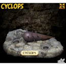 X-Plus Model Kit Cyclops toy figure shown resting on a rocky base against a dark cave-like background, with Cyclops branding and the X-Plus Model Kit logo visible.